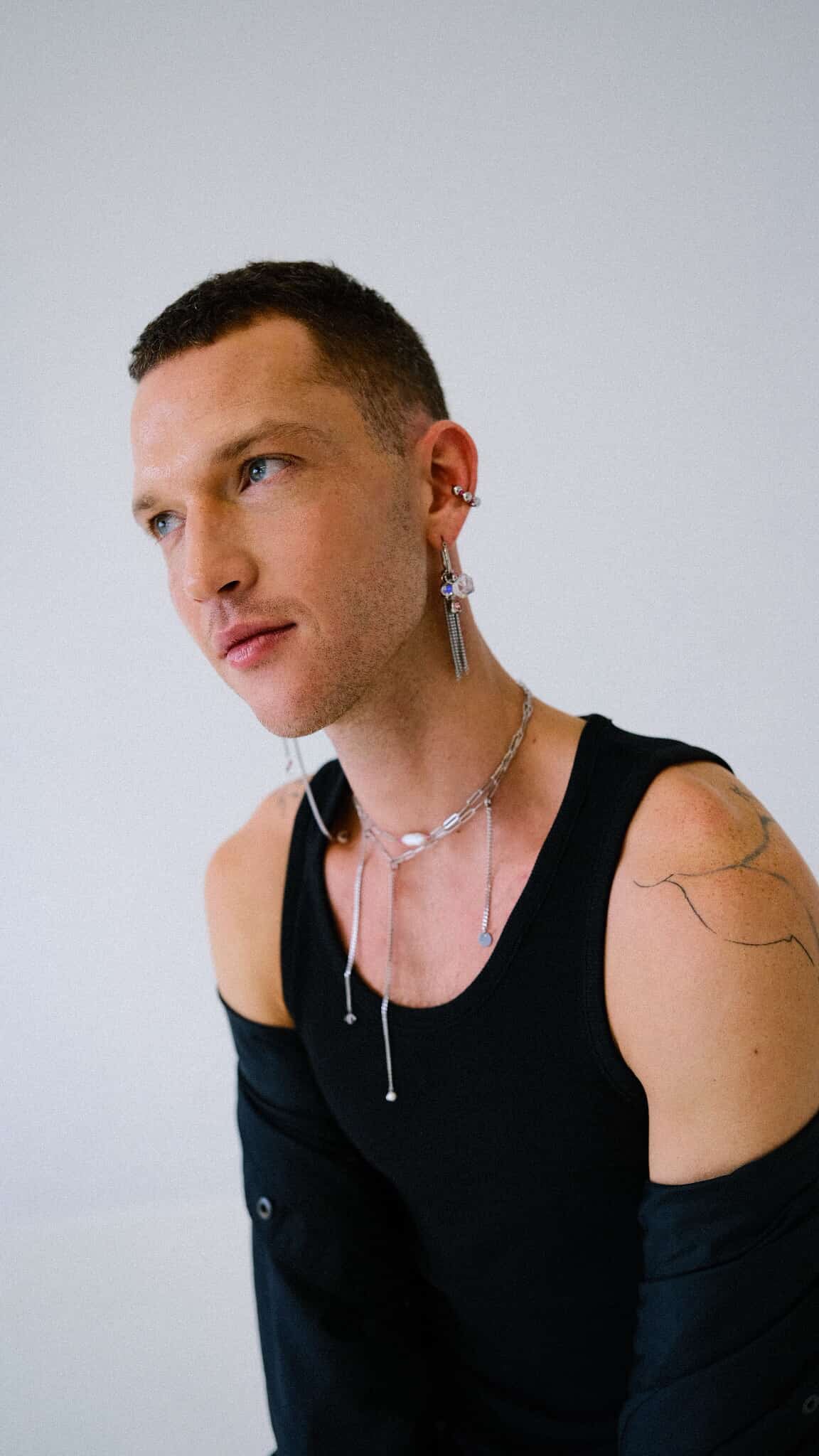 Man wearing a black sleeveless shirt with visible tattoos on his arm against a plain background