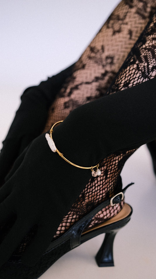 Black high-heeled shoe with a gold bracelet on a white background