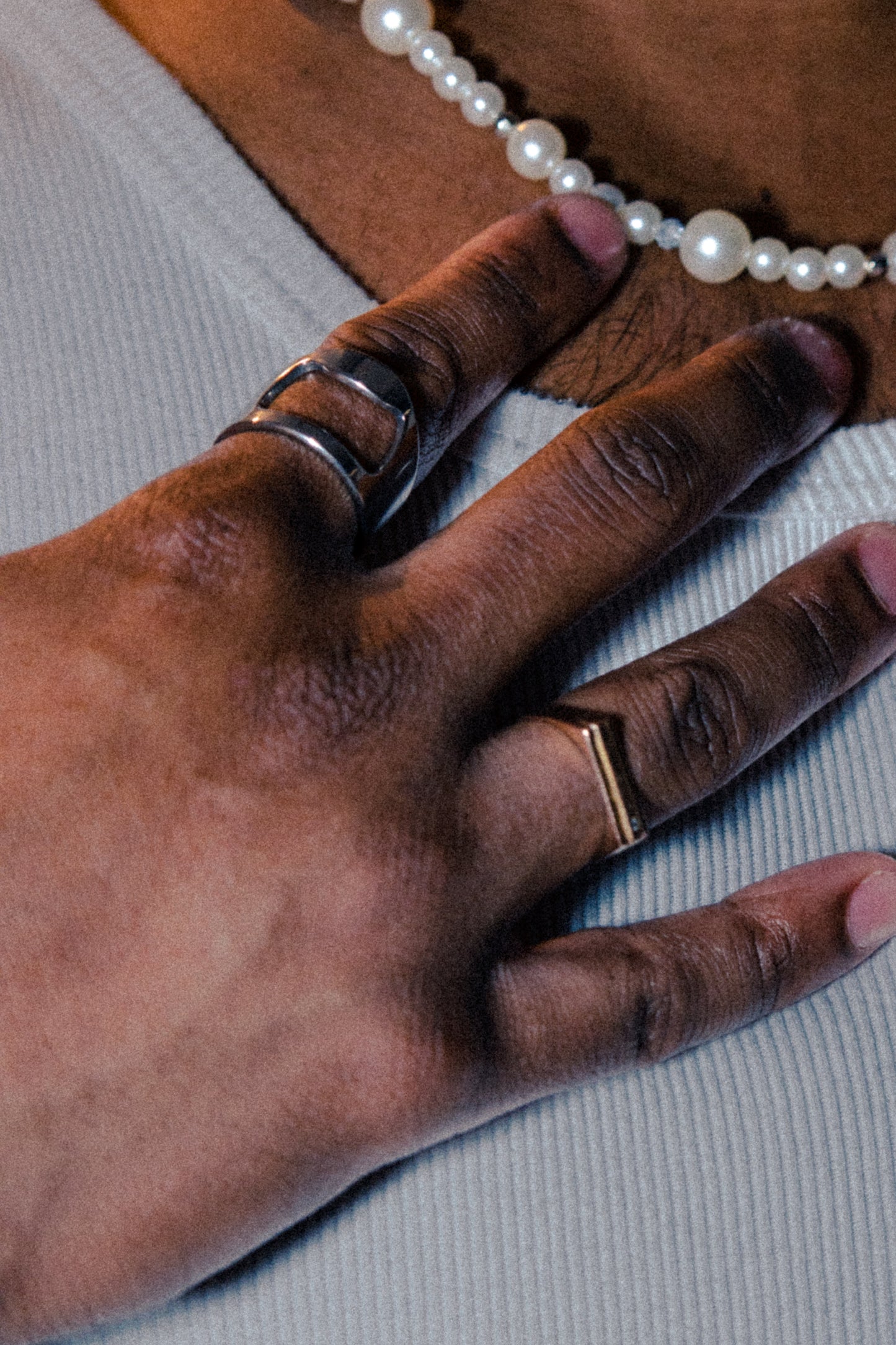 Close-up of a hand wearing the Percé Ring by Sans Régence, a functional stainless steel ring designed with a bottle opener feature. Styled with a pearl necklace and minimalist mixed-metal rings.