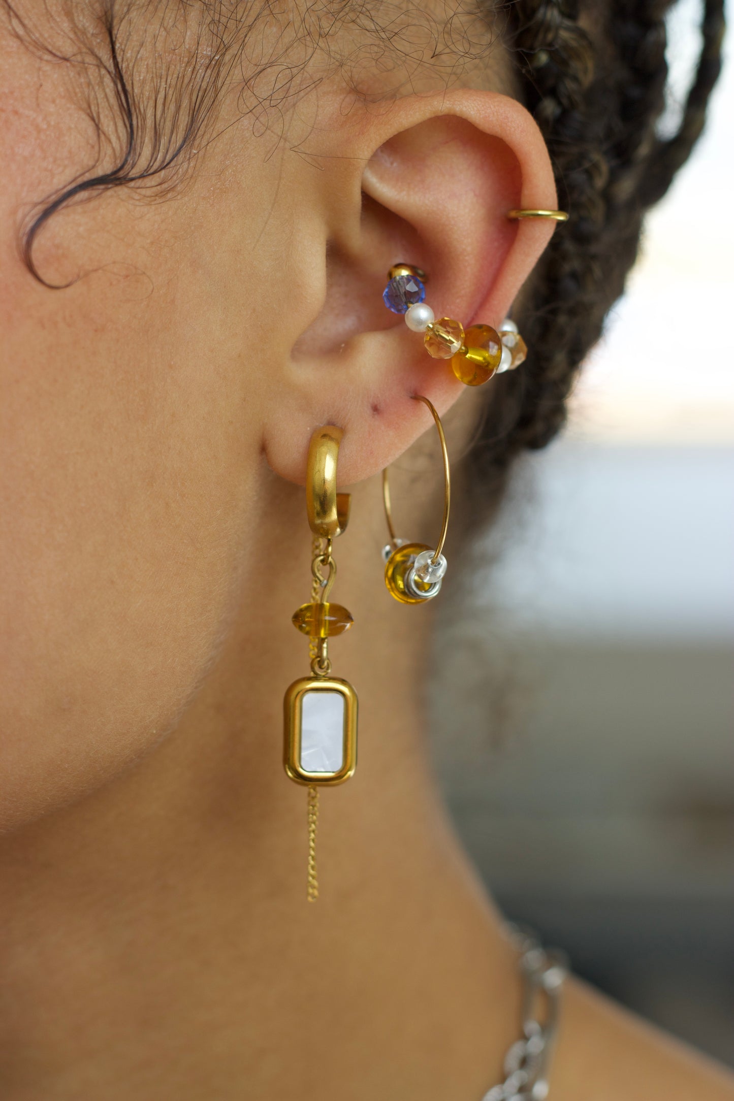 Ear cuff ajustable sans perçage en acier inoxydable plaqué PVD or avec cristaux colorés et perles blanches, porté sur le cartilage de l’oreille dans une composition de bijoux.