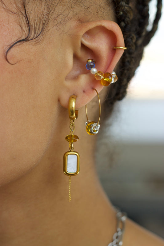 Ear cuff ajustable sans perçage en acier inoxydable plaqué PVD or avec cristaux colorés et perles blanches, porté sur le cartilage de l’oreille dans une composition de bijoux.