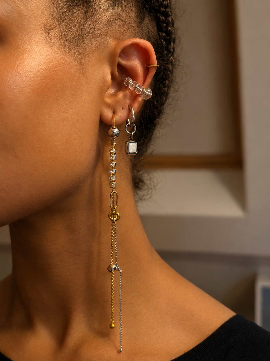 Mono boucle d’oreille longue en acier inoxydable argent et or avec cristaux sertis et chaînes pendantes, vue portée de profil dans une composition d’oreille avec d’autres bijoux.