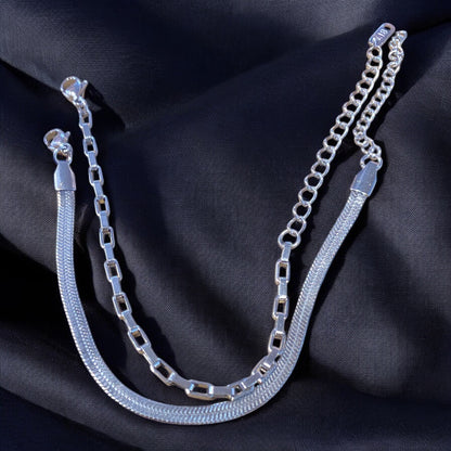 Two stainless steel bracelets, one with a bold box-link chain and the other with a smooth snake chain, displayed on a dark fabric surface.