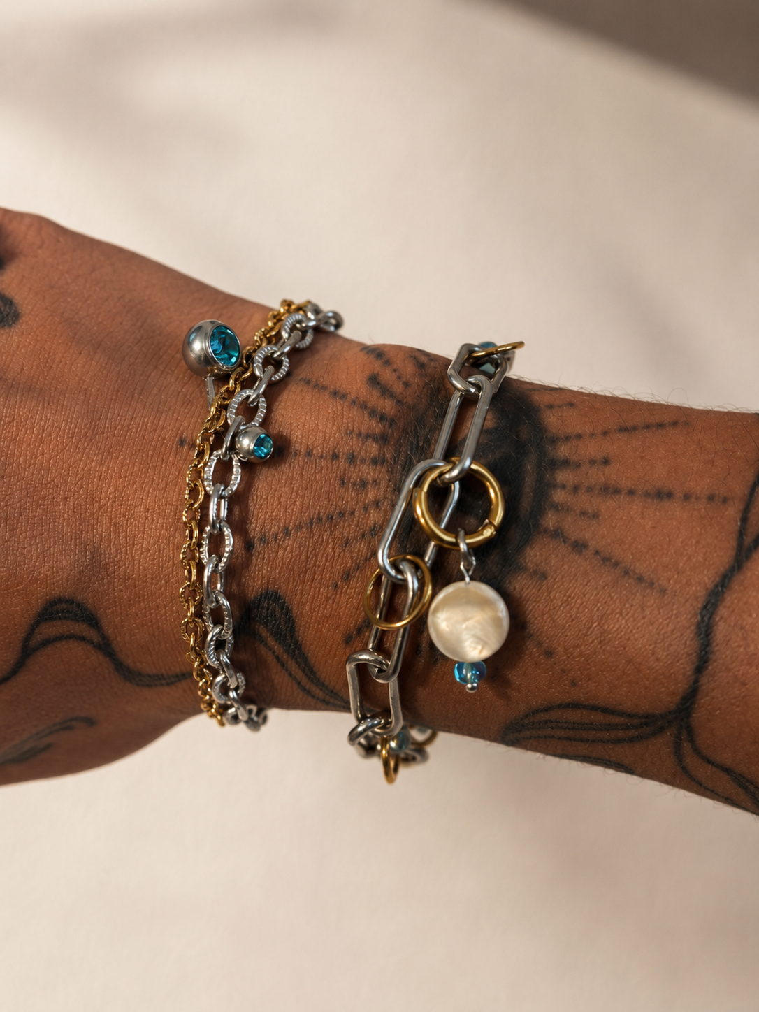 Deux bracelets modulaires Mistral portés au poignet, mélange de chaînes argentées et dorées avec perles naturelles et détails bleus.
