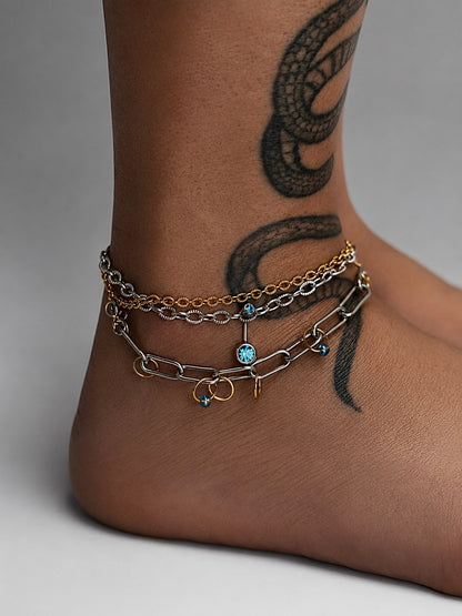 Bracelets modulaires Mistral portés comme bracelets de cheville, acier inoxydable argent et or avec cristaux bleus et anneaux dorés.