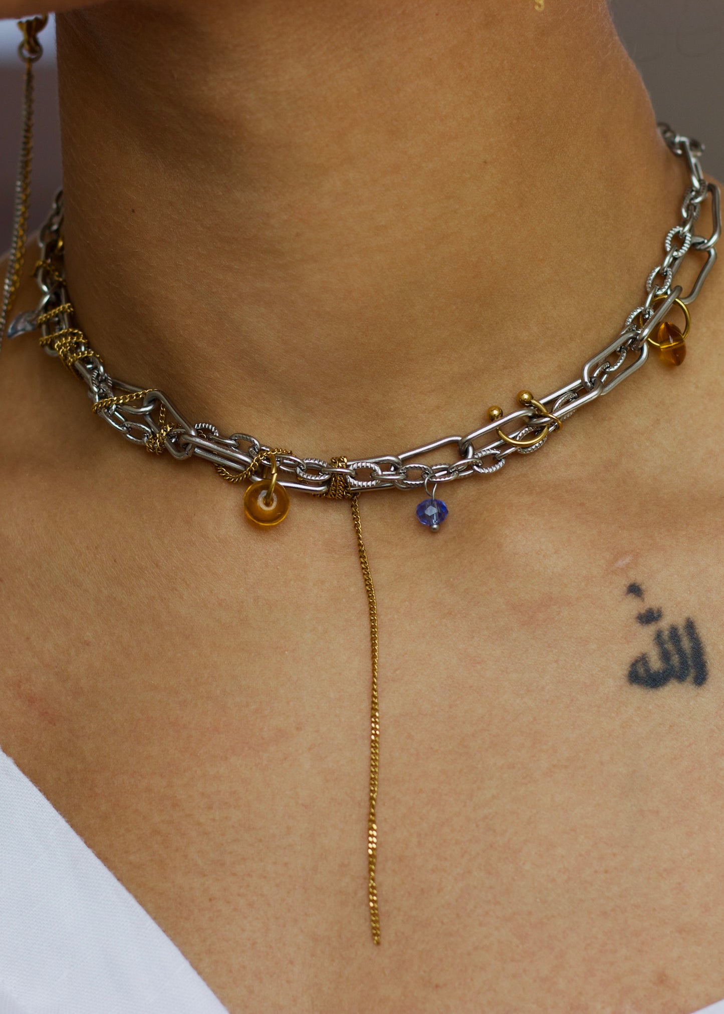 Collier choker en acier inoxydable argent et or avec détails ambrés et breloque violette, porté autour du cou, vue de face.
