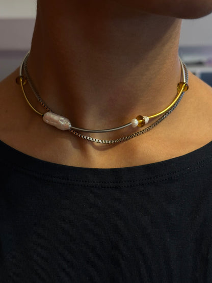 Collier choker en acier inoxydable or et argent avec perle baroque d’eau douce, porté près du cou, vue de face.