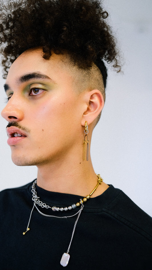 Man with styled hair and multiple necklaces against a neutral background