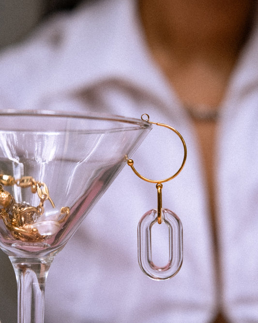 Gold hoop earrings with clear oval pendants near a martini glass.