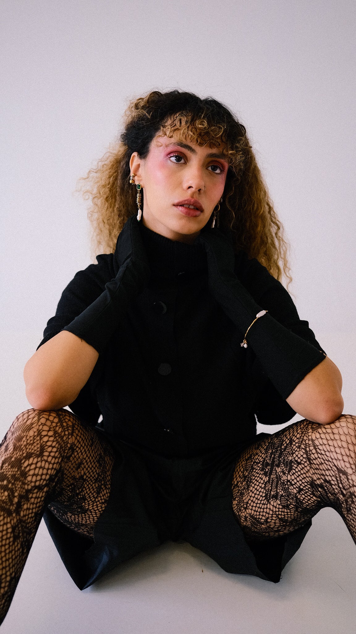 Woman wearing a black outfit with fishnet stockings against a white background
