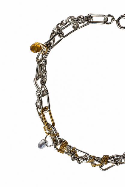 Vue rapprochée sur fond blanc d’un collier choker en acier inoxydable argent et or avec chaînes texturées, breloques translucides et détails industriels.