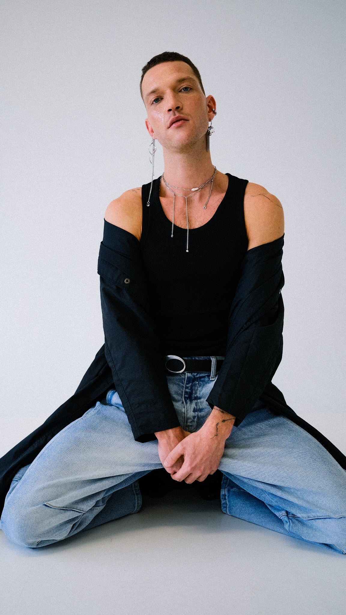 Person wearing a black off-shoulder top and light blue jeans sitting on a white floor.