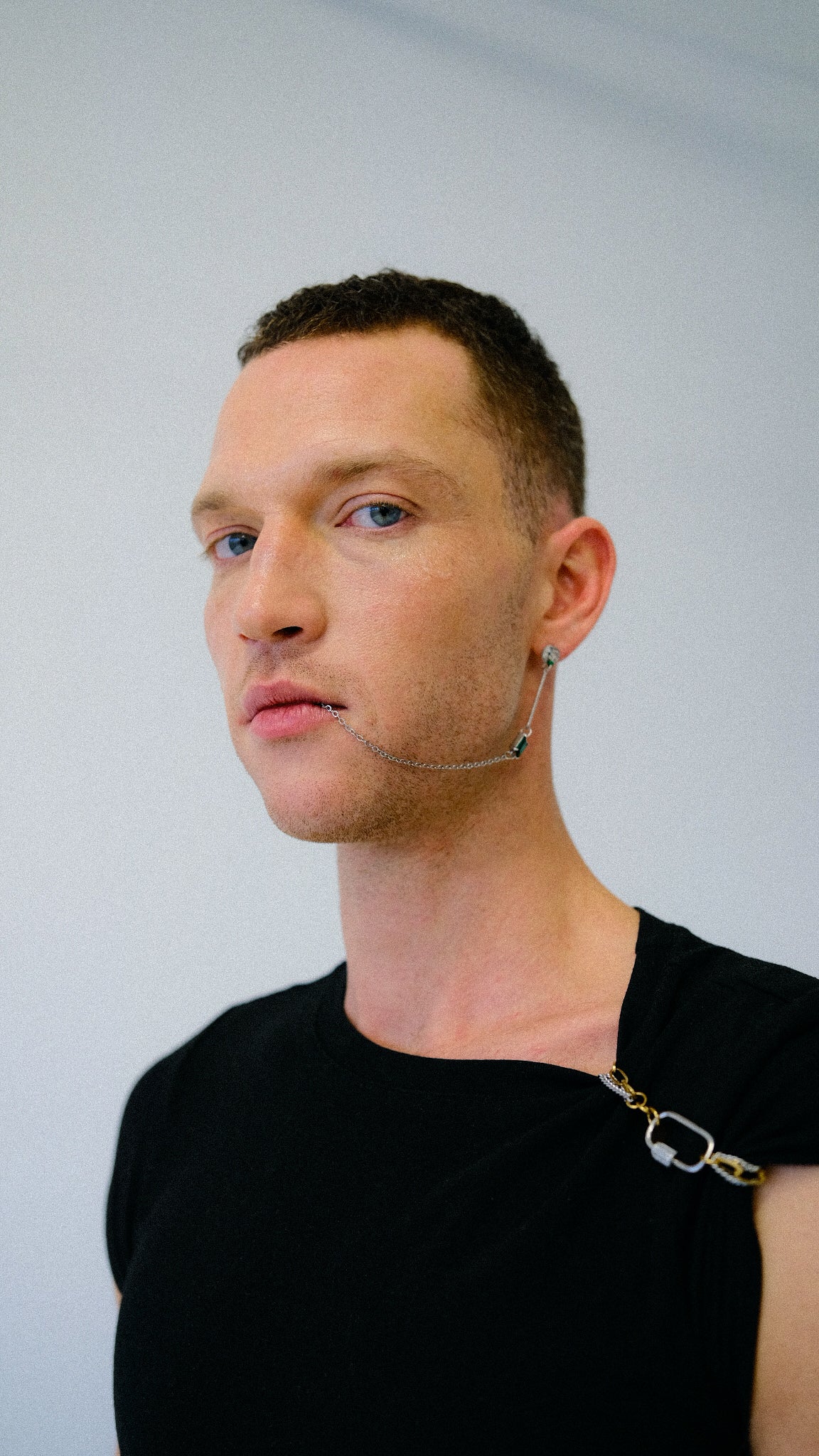 Man wearing a black shirt with a gold chain against a plain background