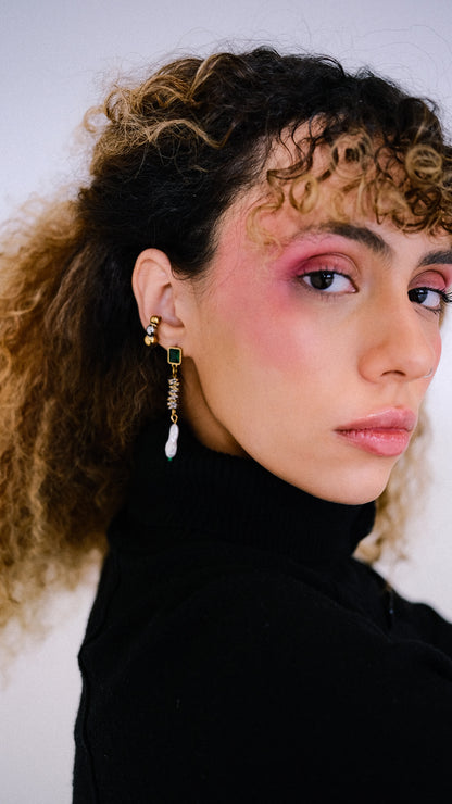 Close-up of a person wearing gold earrings with a white stone against a neutral background