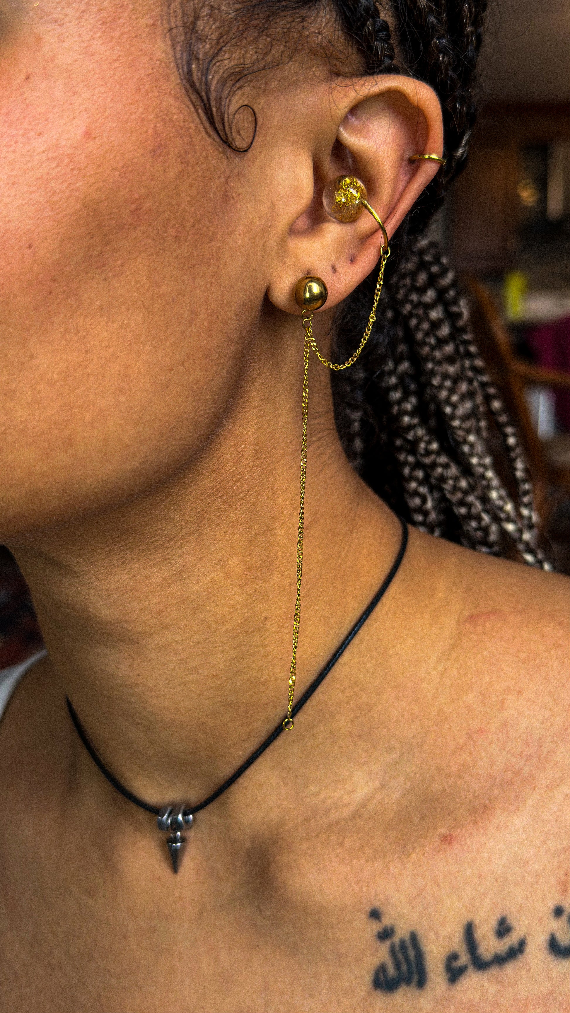 Close-up of an ear with gold earrings and a necklace, with a blurred background.