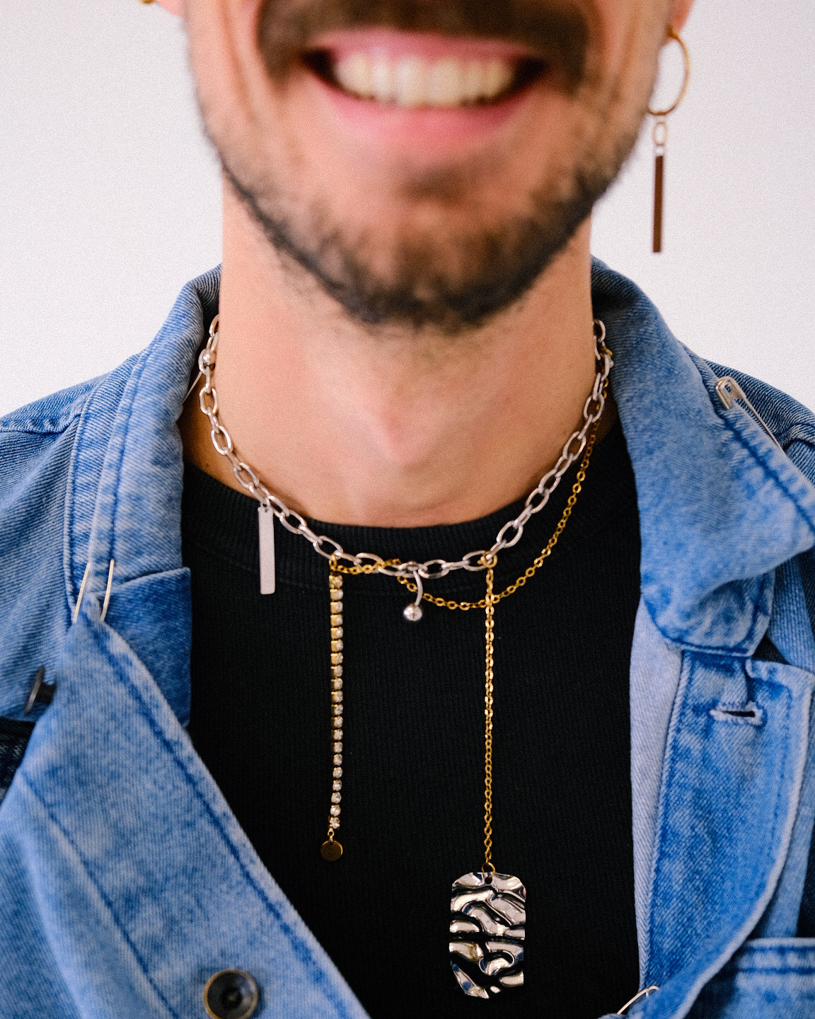 Man wearing multiple necklaces with a denim jacket and black shirt