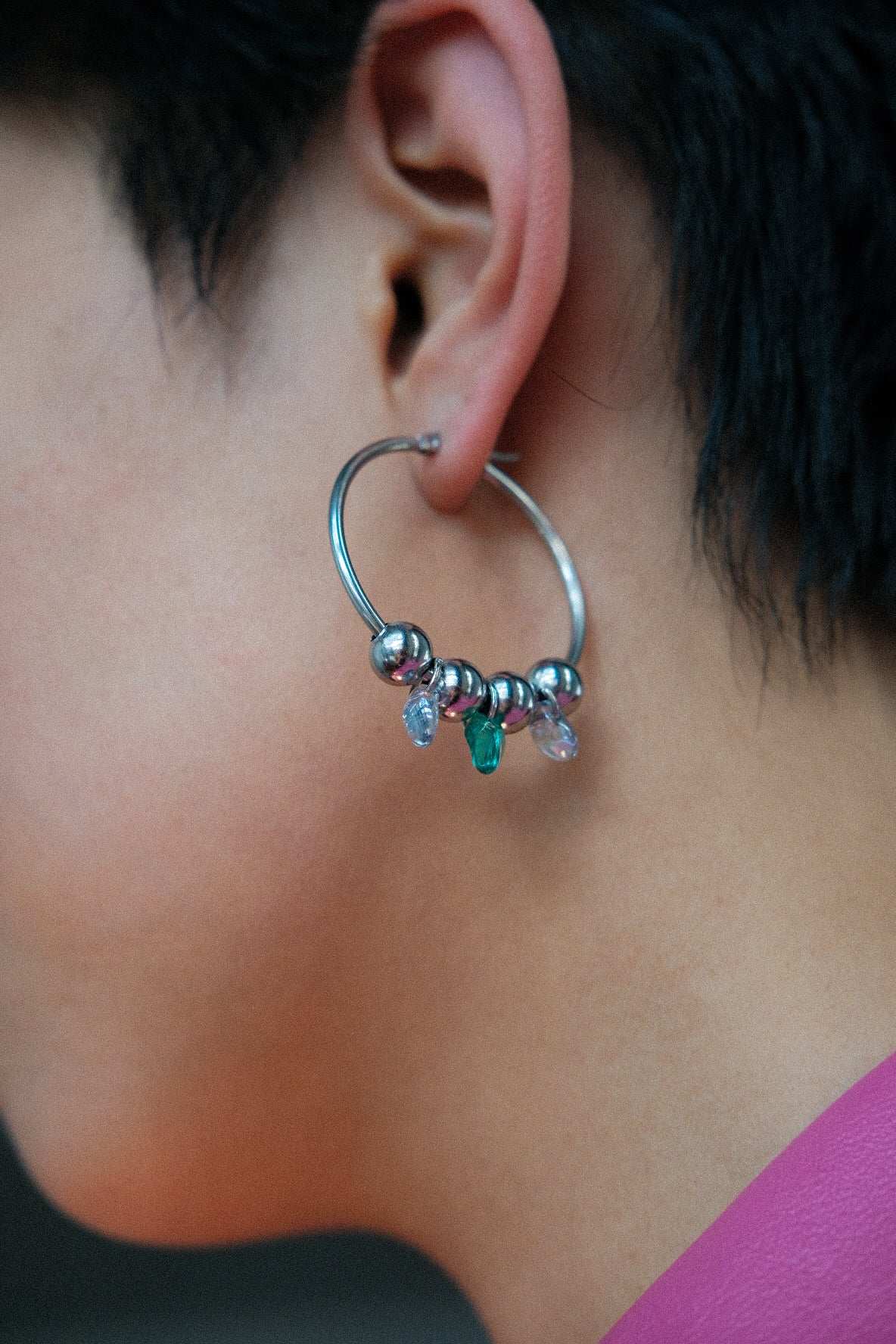Close-up of an ear wearing a silver hoop earring with colorful beads.