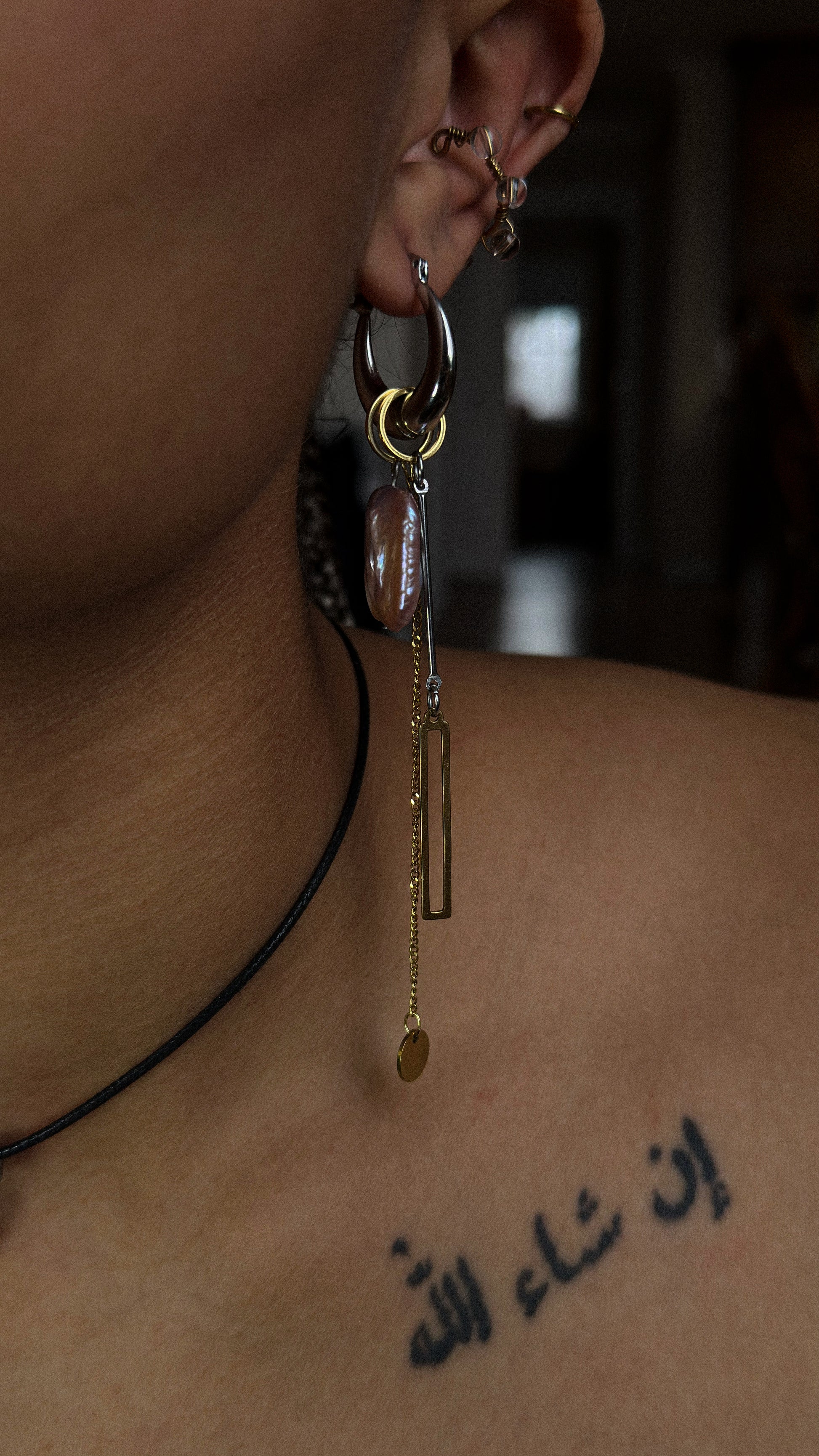 Close-up of an earring with a dangling gold tag on a person's ear, with a tattoo visible on the neck.