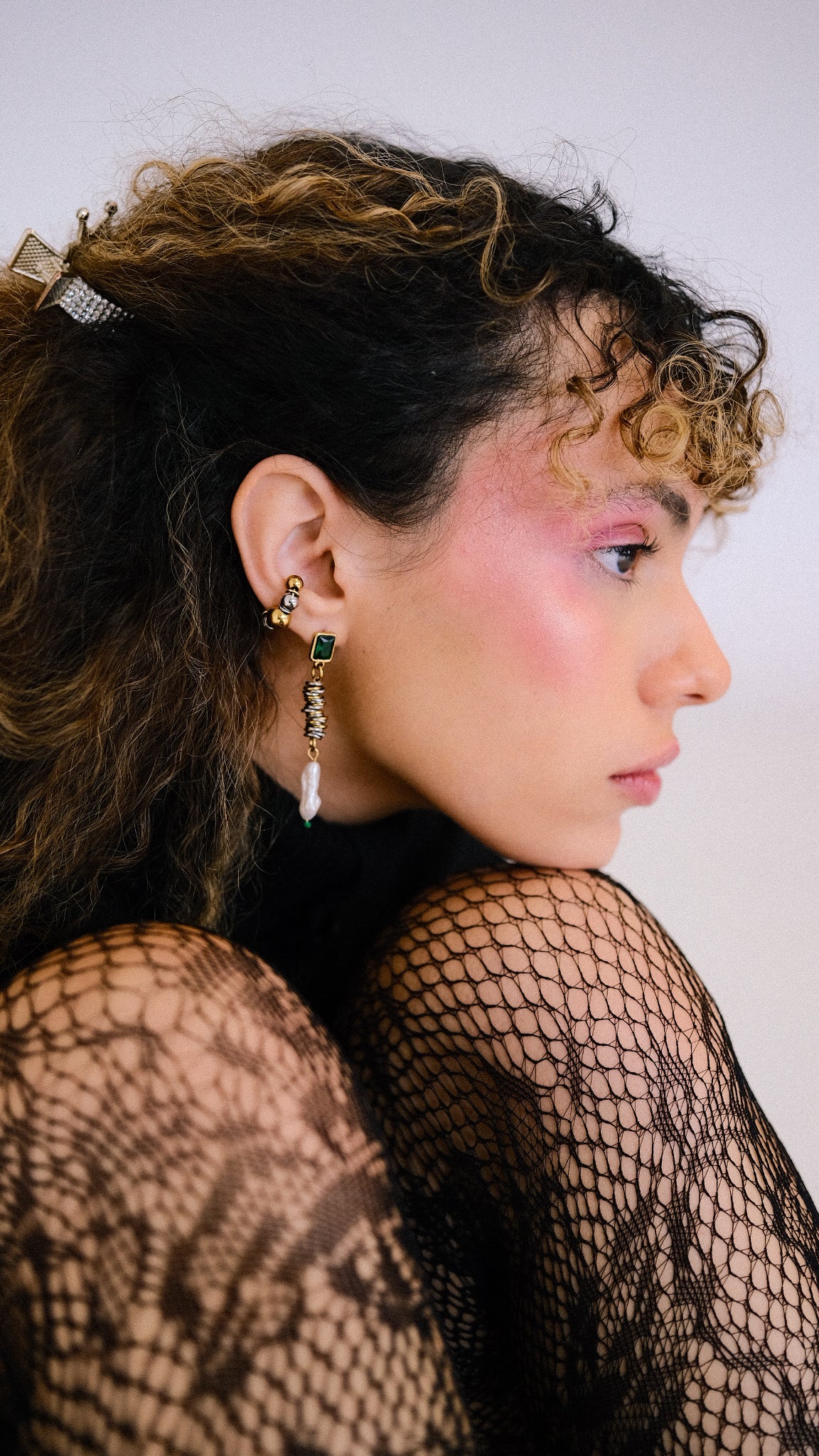 Person wearing fishnet top and earrings with a neutral background